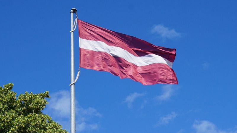Det lettiske flag, med den karakteristiske karmoisinrøde farve og en hvid, horisontal stribe, har rødder helt tilbage til en krønike fra 1279. Farverne blev taget op igen i 1870’erne af den spirende nationale bevægelse, og i 1917 fik flaget sin nuværende form. Det blev officielt nationalflag ved uafhængigheden i 1918, men forbudt under Sovjettiden. Først i 1987 blev det igen tilladt at vise offentligt, og i foråret 1990 genindførtes det som Letlands officielle flag